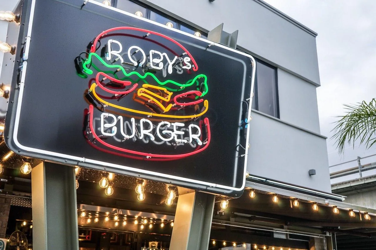 L'insegna al neon di Roby's Burger con le luci a bulbo sopra l'ingresso